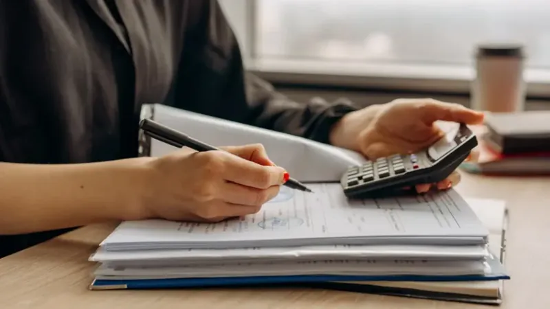 Pessoa fazendo contas com calculadora e papéis