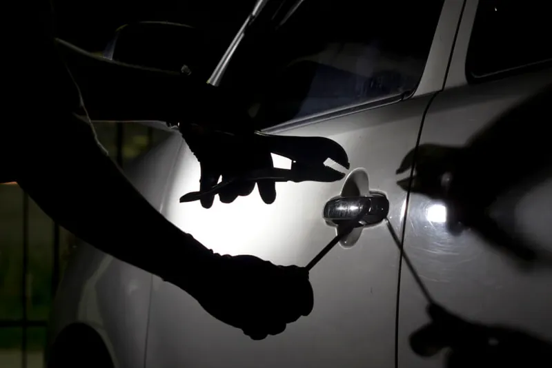 Pessoa forçando a porta de um carro à noite